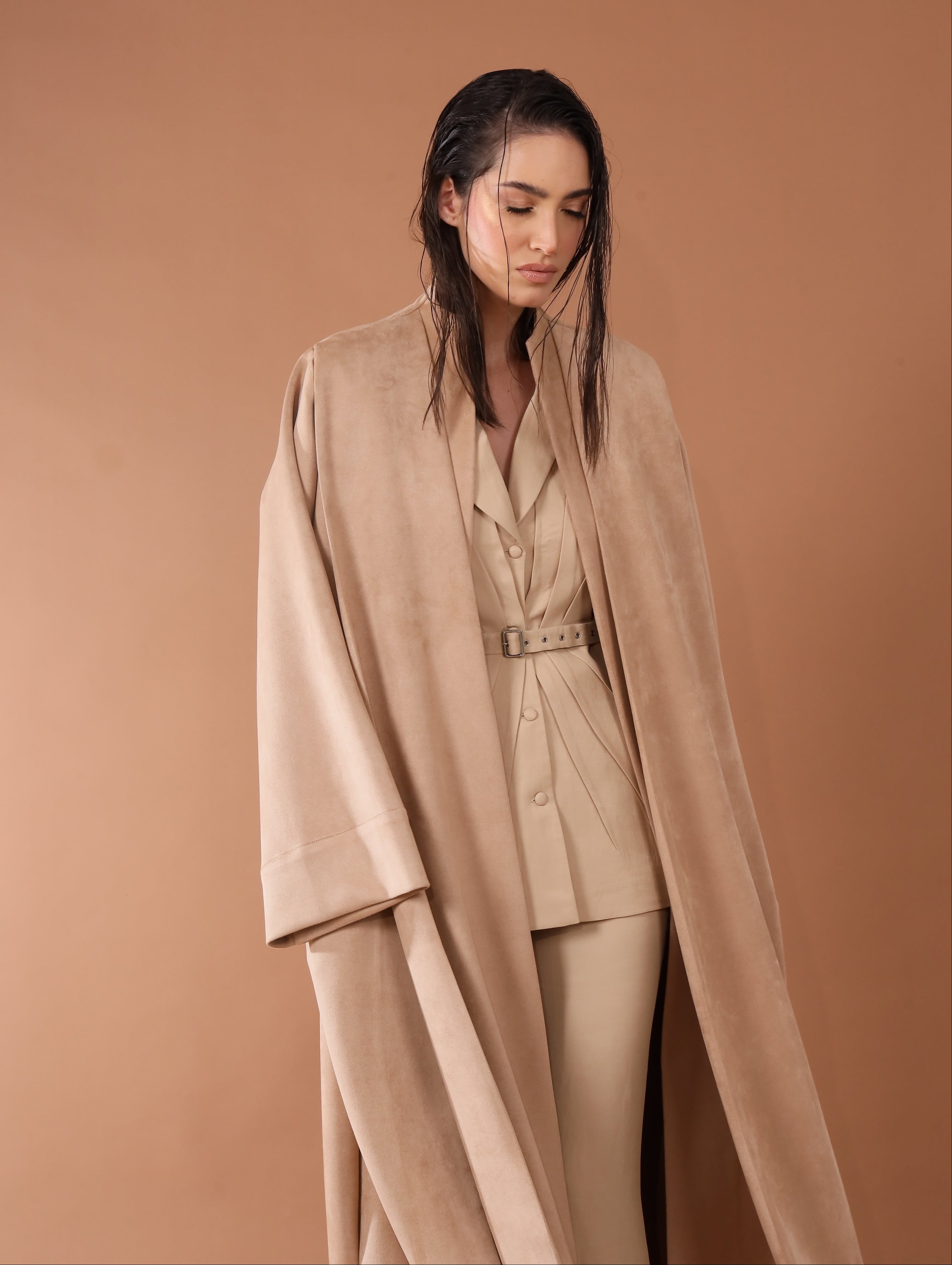 Woman wearing a beige suit with a long coat against a brown background