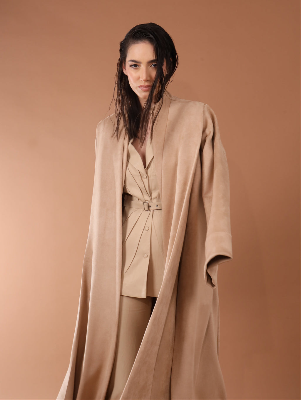 Woman wearing a beige coat and pants against a brown background