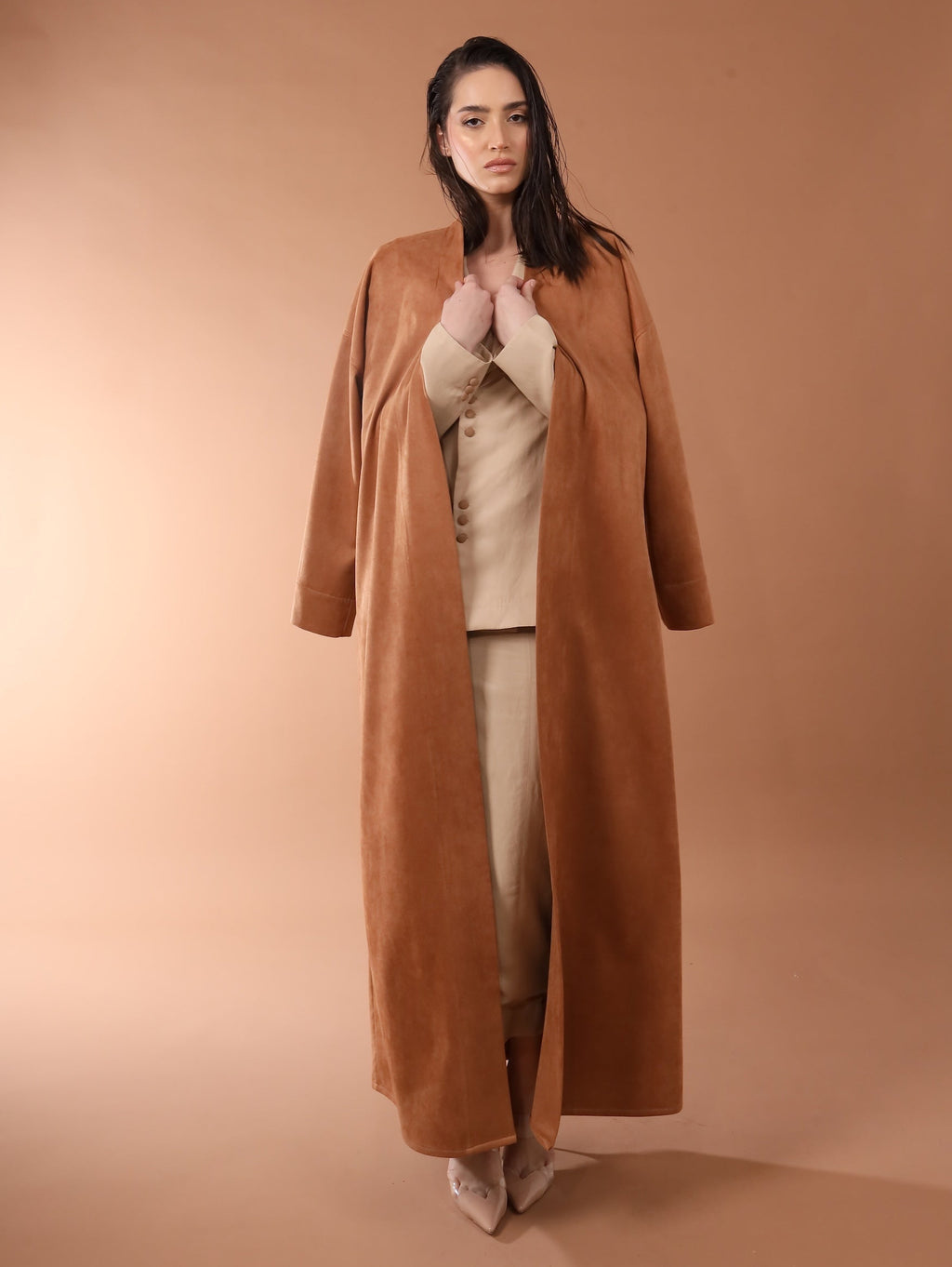 Woman wearing a long brown coat in front of a beige backdrop