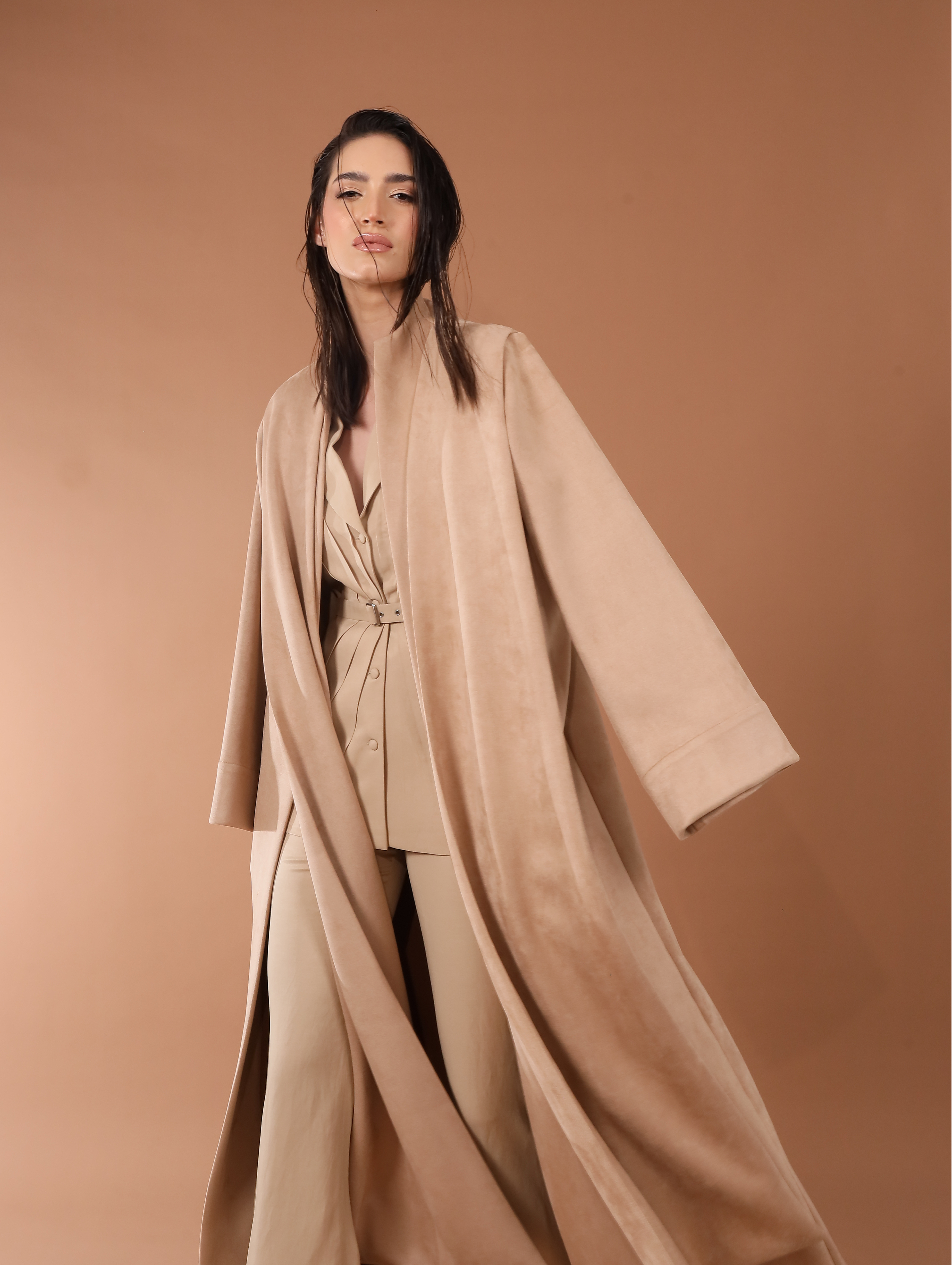 Woman wearing a beige outfit against a brown background